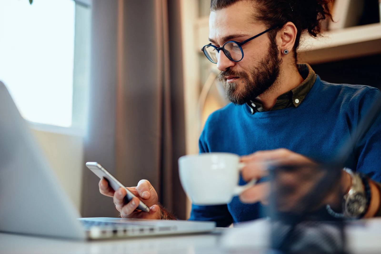 Professional researching on a laptop while holding a smartphone and coffee